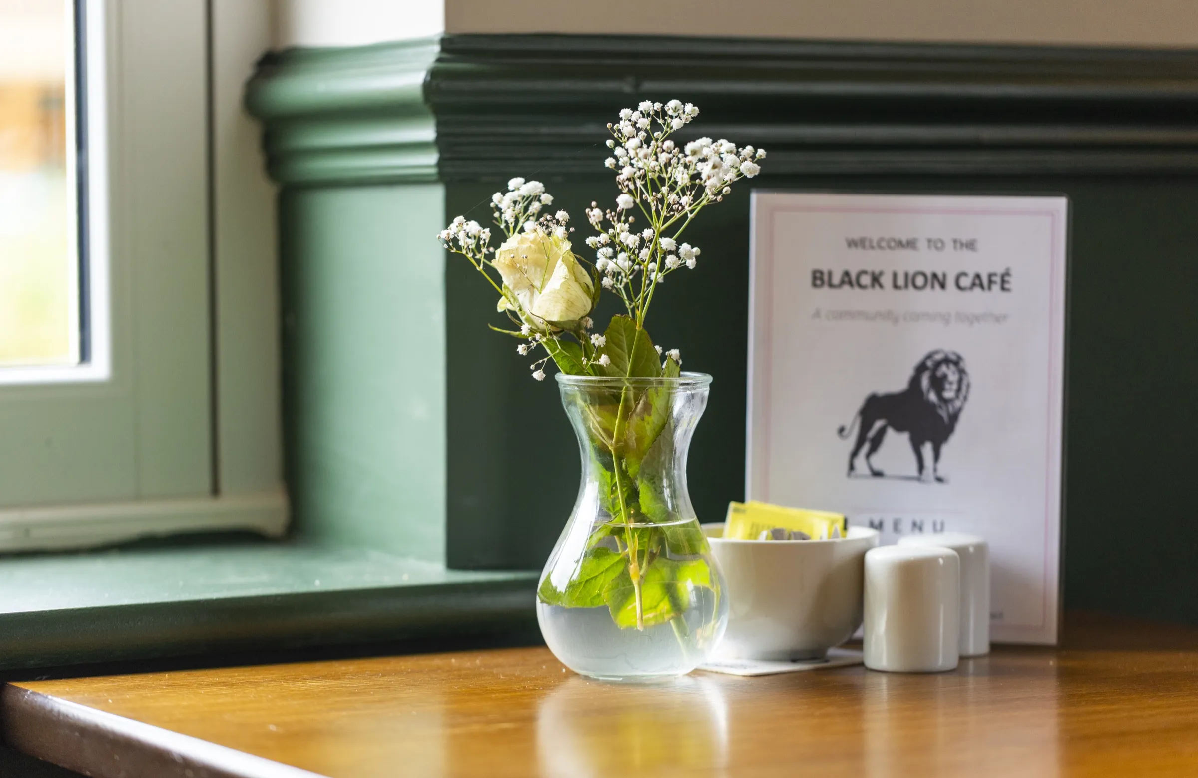 A café table set with flowers, salt and the Black Lion menu