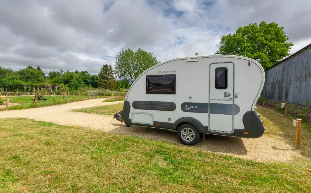 Adria Action touring caravan on a gravel pitch beside the barn