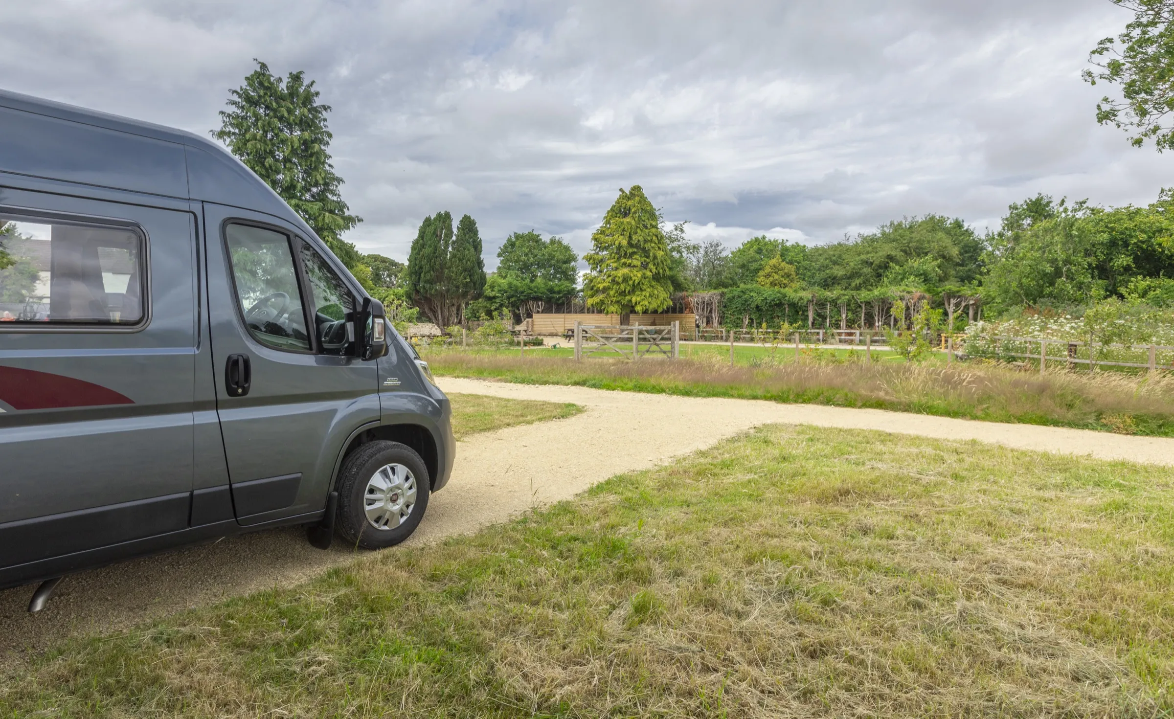 A motorhome on a gravel pitch looking out to fields and trees