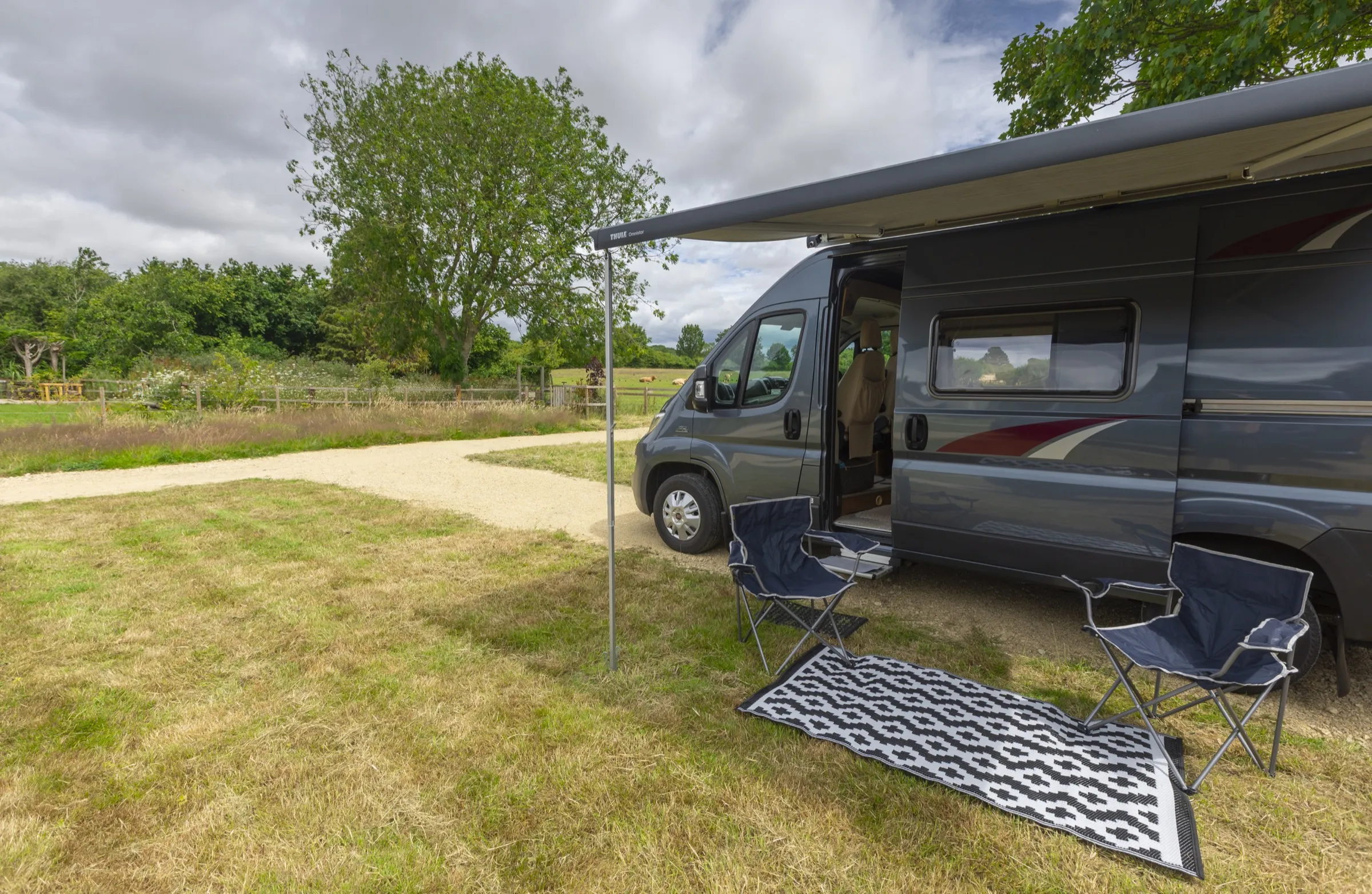 Campervan with awning, chairs and rug on a pitch looking toward the fields