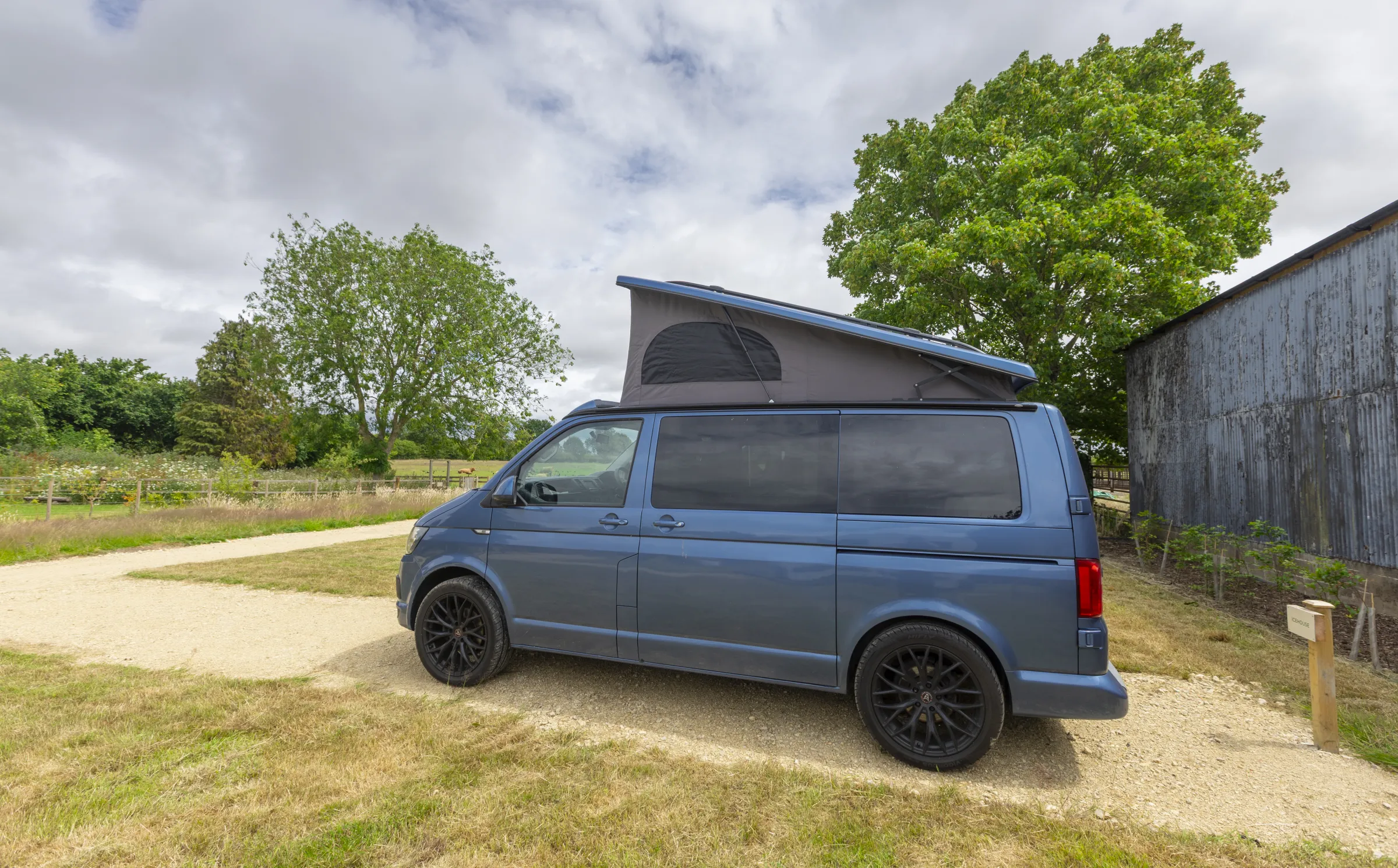 Blue Volkswagen campervan with pop-top raised beside the barn