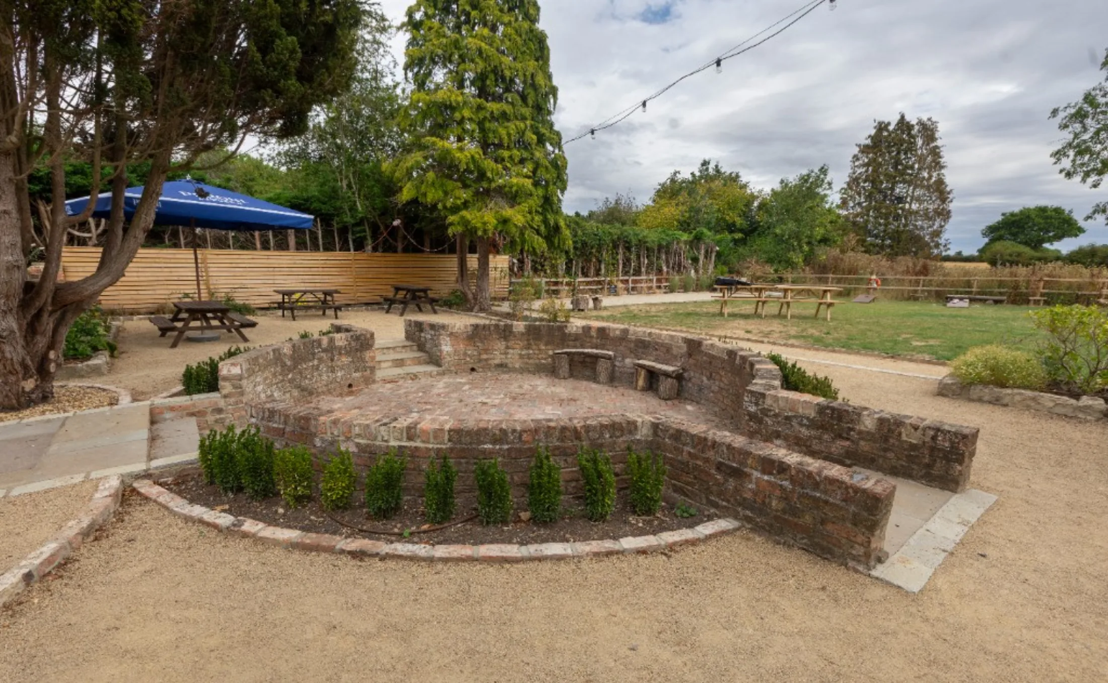 The beer garden at The Black Lion, with picnic tables, lawn and a brick seating nook